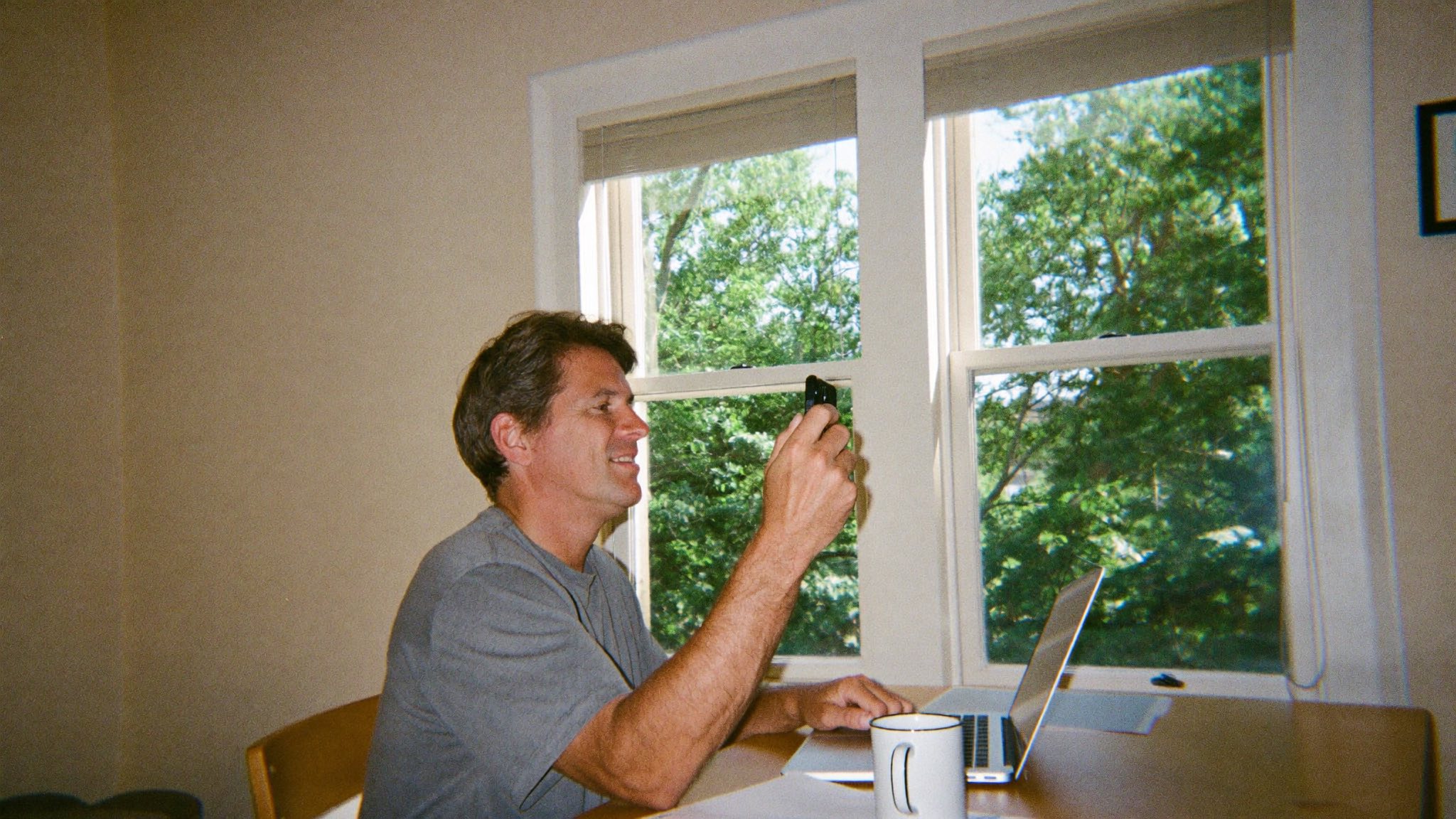 A man at a sunlit kitchen table replying on his phone the moment the lead comes in